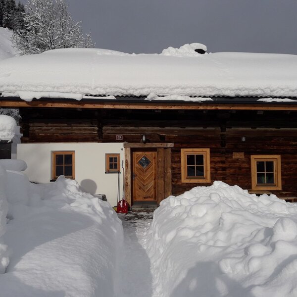 The Alpine Hut exterior in a snowy mountain setting, with a cleared path leading to the entrance.