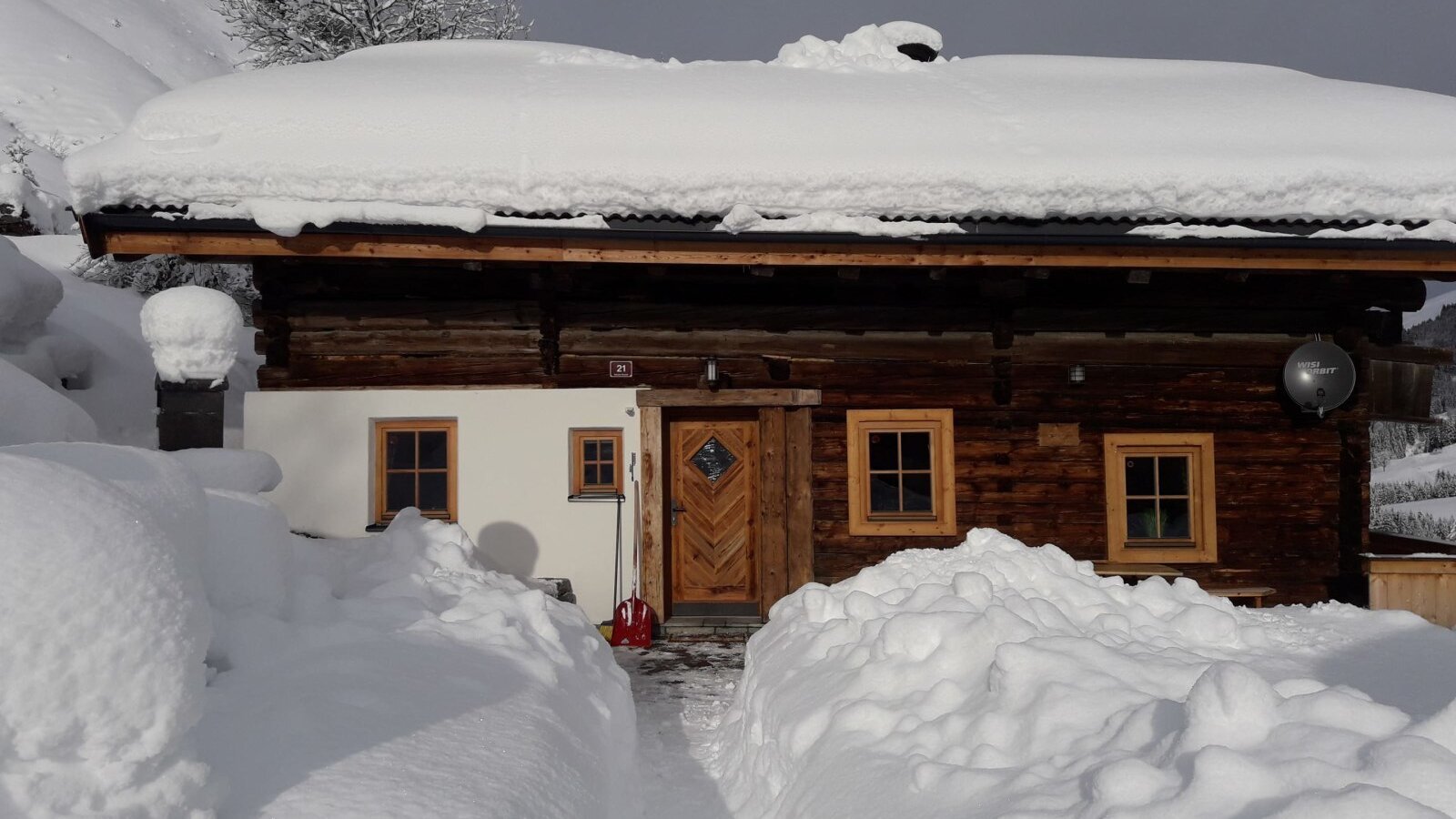 The Alpine Hut exterior in a snowy mountain setting, with a cleared path leading to the entrance.