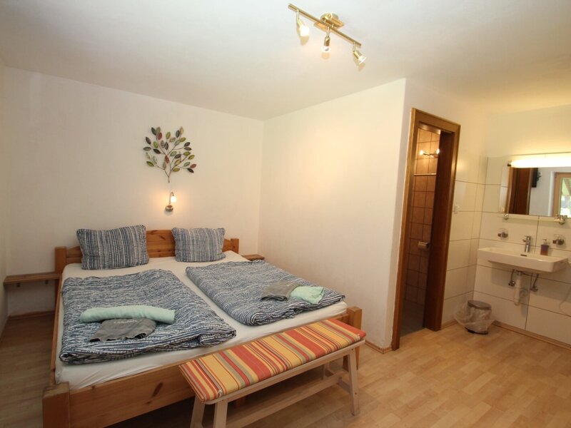 A guest bedroom in the Farm House featuring a double bed, a wall-mounted TV, and an adjacent bathroom area with a sink, mirror, and separate shower/WC.
