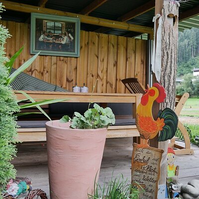 The covered outdoor seating area at the Farm House features wooden furniture, potted plants, and a view of the hills.