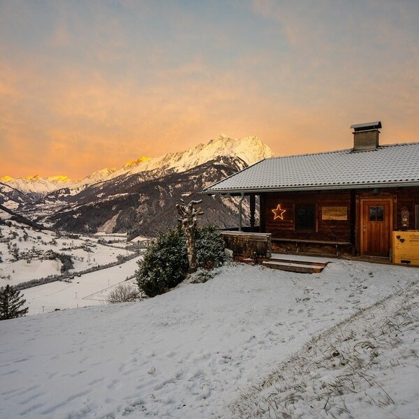 The Farm House exterior, a wooden structure with a snow-covered roof, overlooks a snowy mountain valley with sunlit peaks. The Farm House exterior, a wooden structure with a snow-covered roof, overlooks a snowy mountain valley with sunlit peaks.