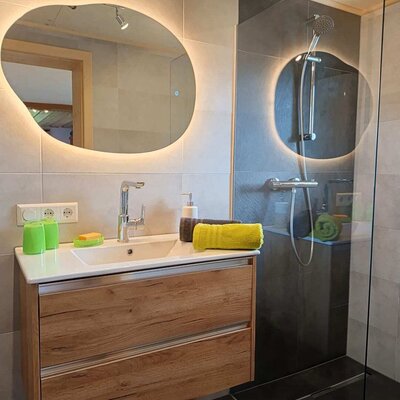 Modern bathroom in the farmhouse with a vanity sink, illuminated mirror, and walk-in shower.