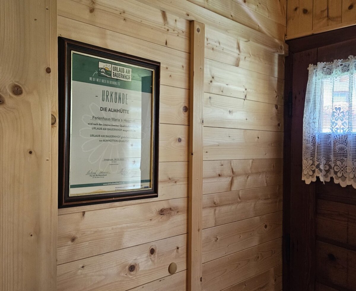 The rustic wooden wall in the  farmhouse, featuring a framed certificate next to a traditional lace curtain.