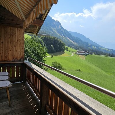 An inviting balcony featuring cozy wooden chairs and a spectacular view over the lush green hills and valley.