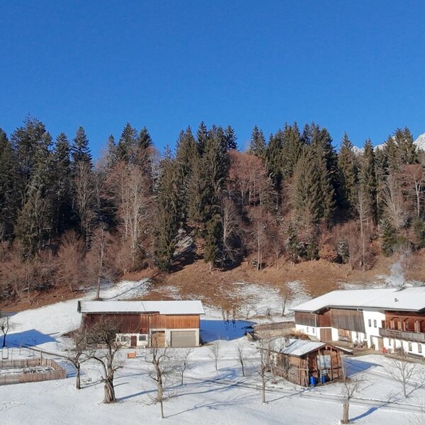 The farmhouse in winter, surrounded by snow, forest, and mountains.