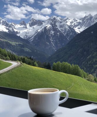 A cup of coffee on the farmhouse balcony with sweeping views of the green hills and snow-capped mountain peaks.