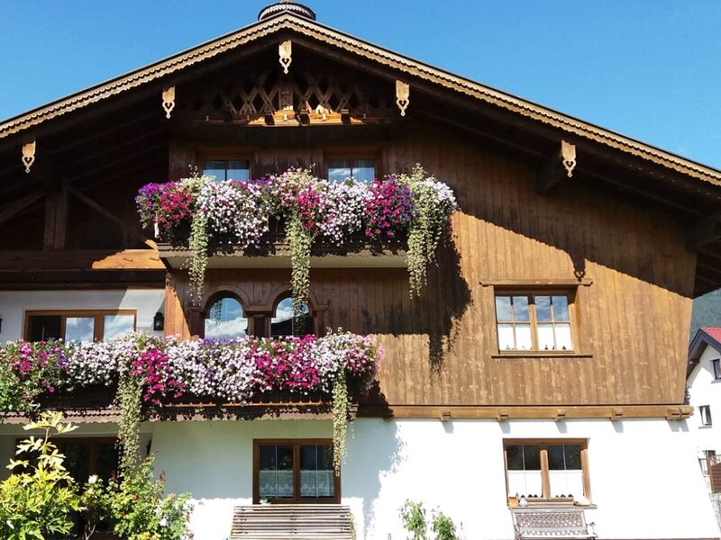 The exterior of the Farm House, featuring wooden balconies abundant with flowering plants.