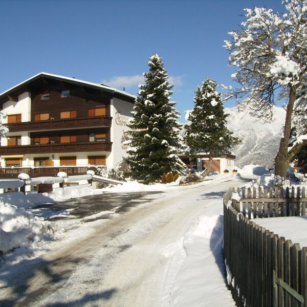 The Farm House exterior in winter, featuring balconies, snow-covered trees, and a mountain backdrop.
