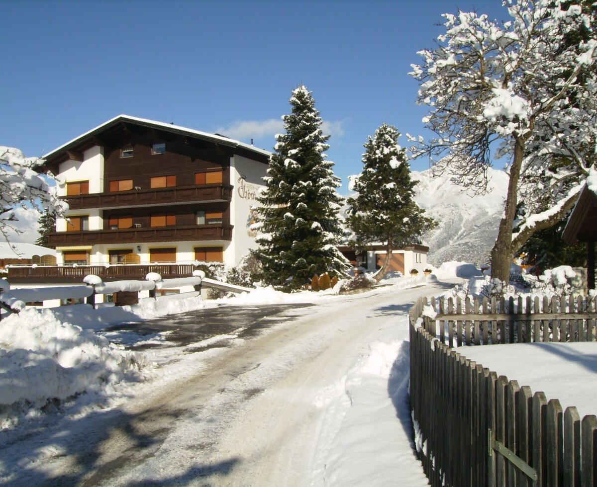 The Farm House exterior in winter, featuring balconies, snow-covered trees, and a mountain backdrop.