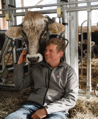 The farmer is stroking a cow in the barn.
