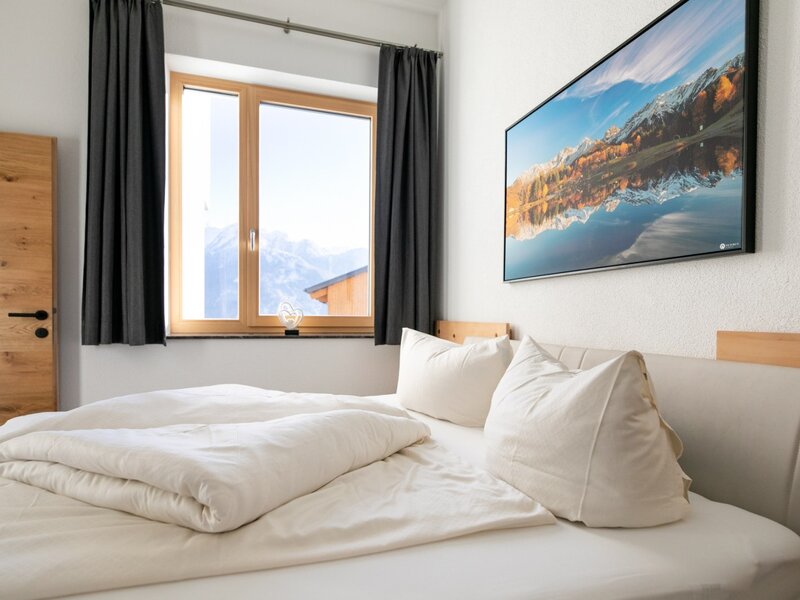 Bedroom in the holiday apartment with a double bed, window offering mountain views, and a wooden door.