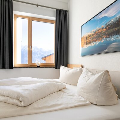 Bedroom in the holiday apartment with a double bed, window offering mountain views, and a wooden door.