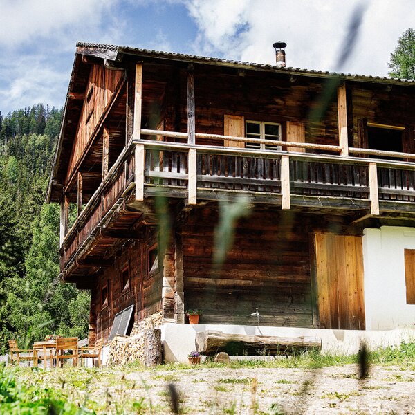 The Alpine Hut, a wooden structure with a balcony, is set amidst a forest and includes an outdoor seating area for guests.
