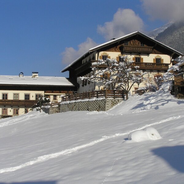 The Farm House exterior in winter, featuring traditional architecture with balconies, surrounded by snow-covered grounds and distant mountains. The Farm House exterior in winter, featuring traditional architecture with balconies, surrounded by snow-covered grounds and distant mountains.