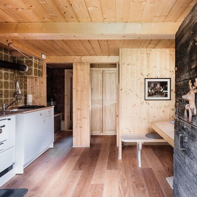 The Alpine Hut features a kitchen equipped with a traditional range cooker, sink, and white cabinets, adjacent to a dining area with a wooden bench and table.