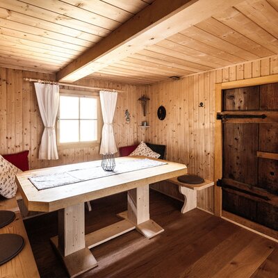 The dining area in the Alpine Hut features a wooden table, built-in bench seating, and wood-paneled walls.