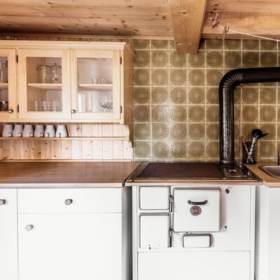 The Alpine Hut kitchen features a wood-burning stove, a sink, and wooden cabinetry with glass-fronted wall units.
