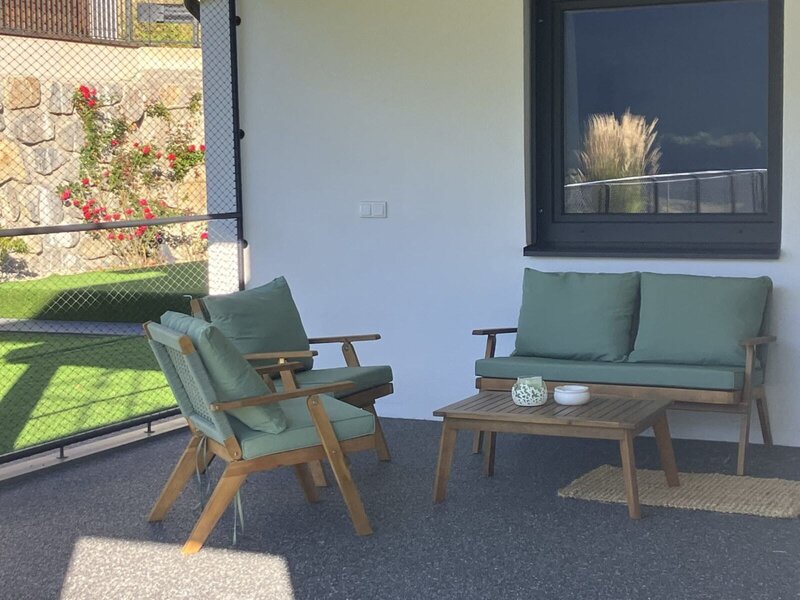 An inviting, covered terrace of the bed and breakfast with comfortable wooden furniture and green cushions for relaxing.
