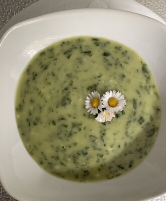 Green soup with darker green flecks, garnished with white daisy flowers, served at the Farm House.