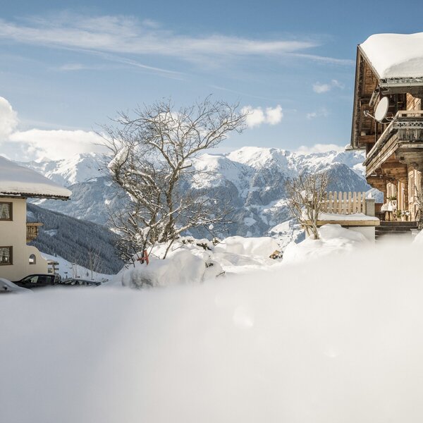 The snowy exterior of the Farm House "Hanserhof", featuring traditional wooden architecture against a backdrop of snow-covered mountains.