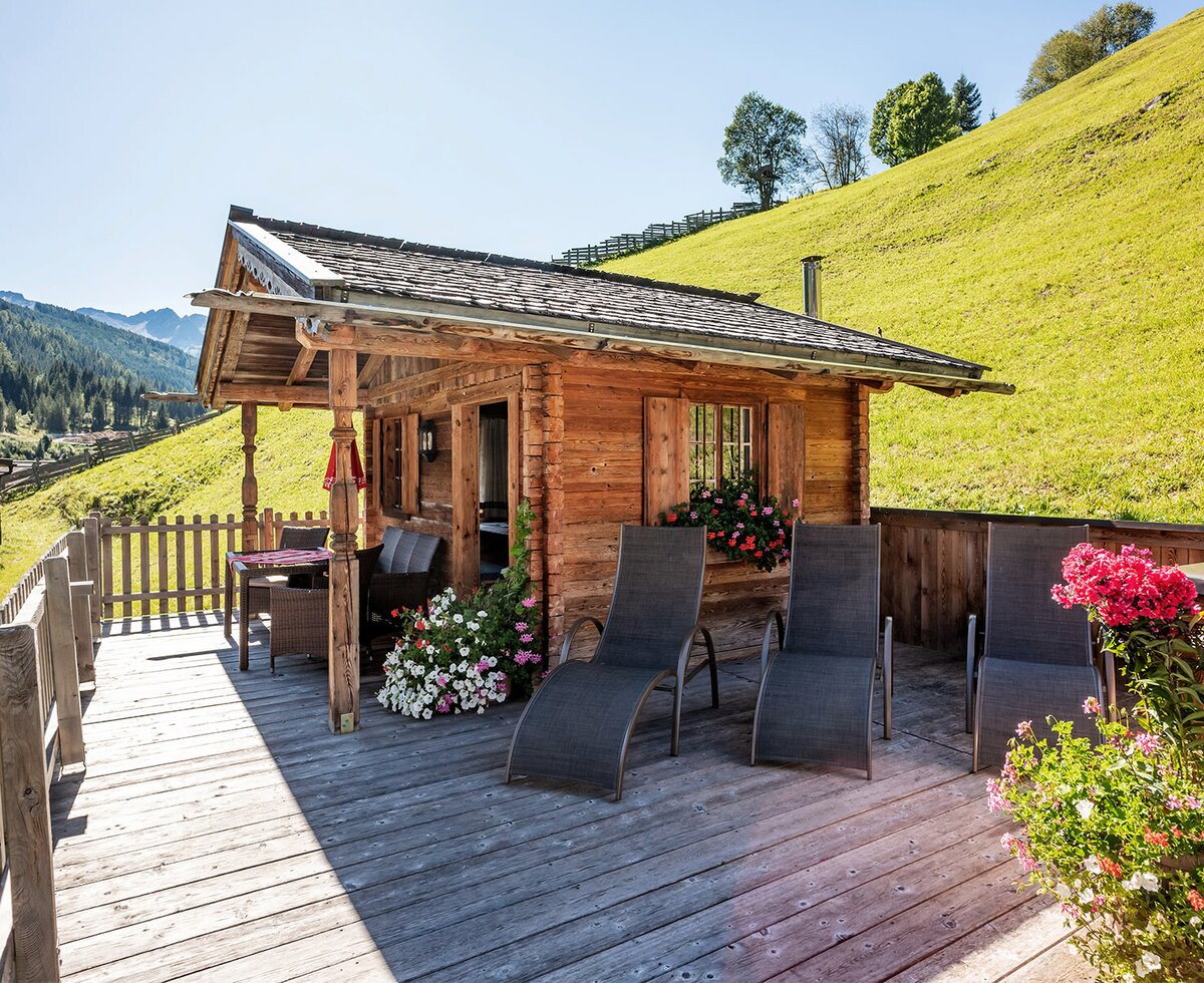 The Farm House offers a wooden deck equipped with sun loungers and an outdoor dining area, set against hillside and mountain scenery.