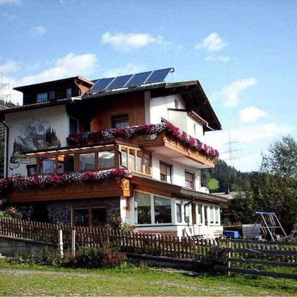 The exterior of the Farm House, featuring balconies with flower boxes, a ground-floor conservatory, solar panels on the roof, and a children's playground in the garden.