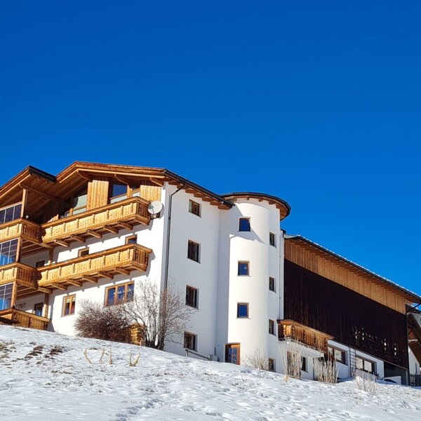 The Bauernhof in winter, with a white facade, wooden cladding, and balconies, situated on a snow-covered hill. The Bauernhof in winter, with a white facade, wooden cladding, and balconies, situated on a snow-covered hill.