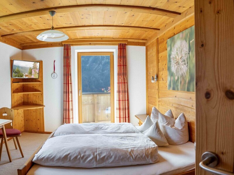 Bedroom in the farmhouse with two single beds, wood paneling, TV, and balcony access.