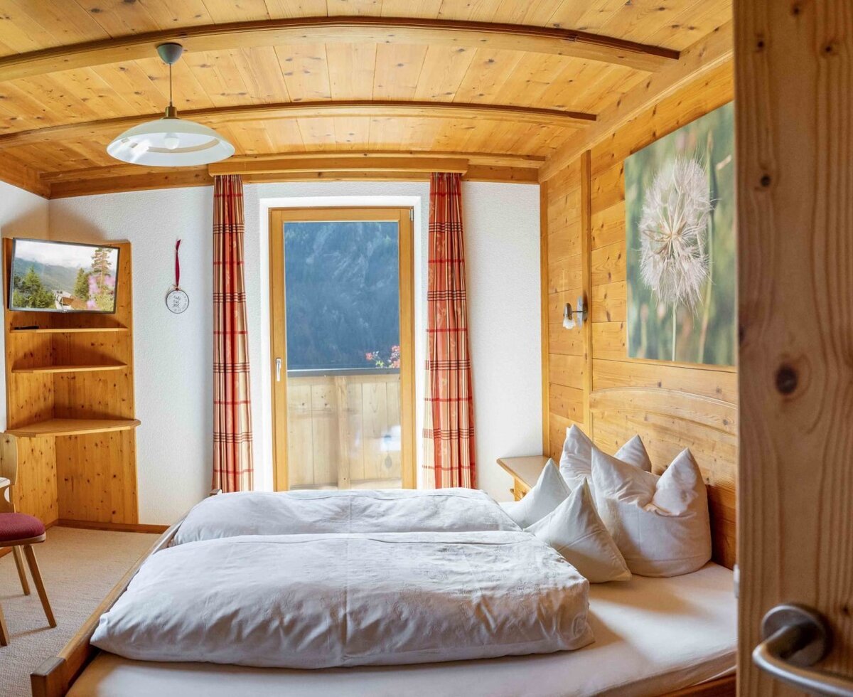 Bedroom in the farmhouse with two single beds, wood paneling, TV, and balcony access.