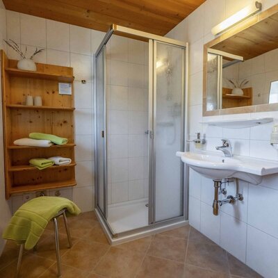 Bathroom in the farmhouse with a shower cabin, sink, mirror, and wooden shelf for towels.