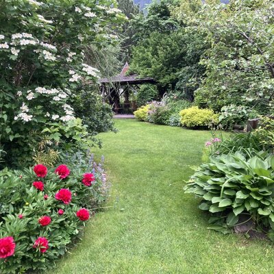 The Farm House garden features a lawn pathway bordered by peonies and other plants, leading to a wooden gazebo.