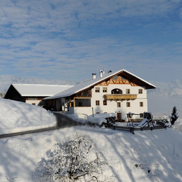 The farm house exterior in winter, featuring snow-covered grounds and distant mountains.
