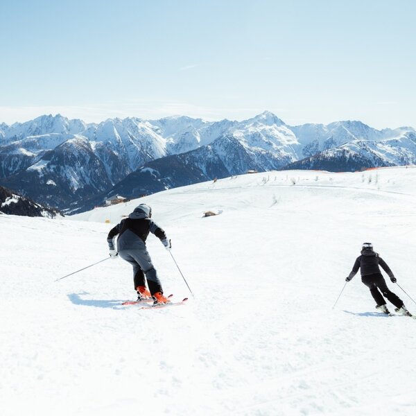 Two people skiing on a snowy slope with a mountain panorama.