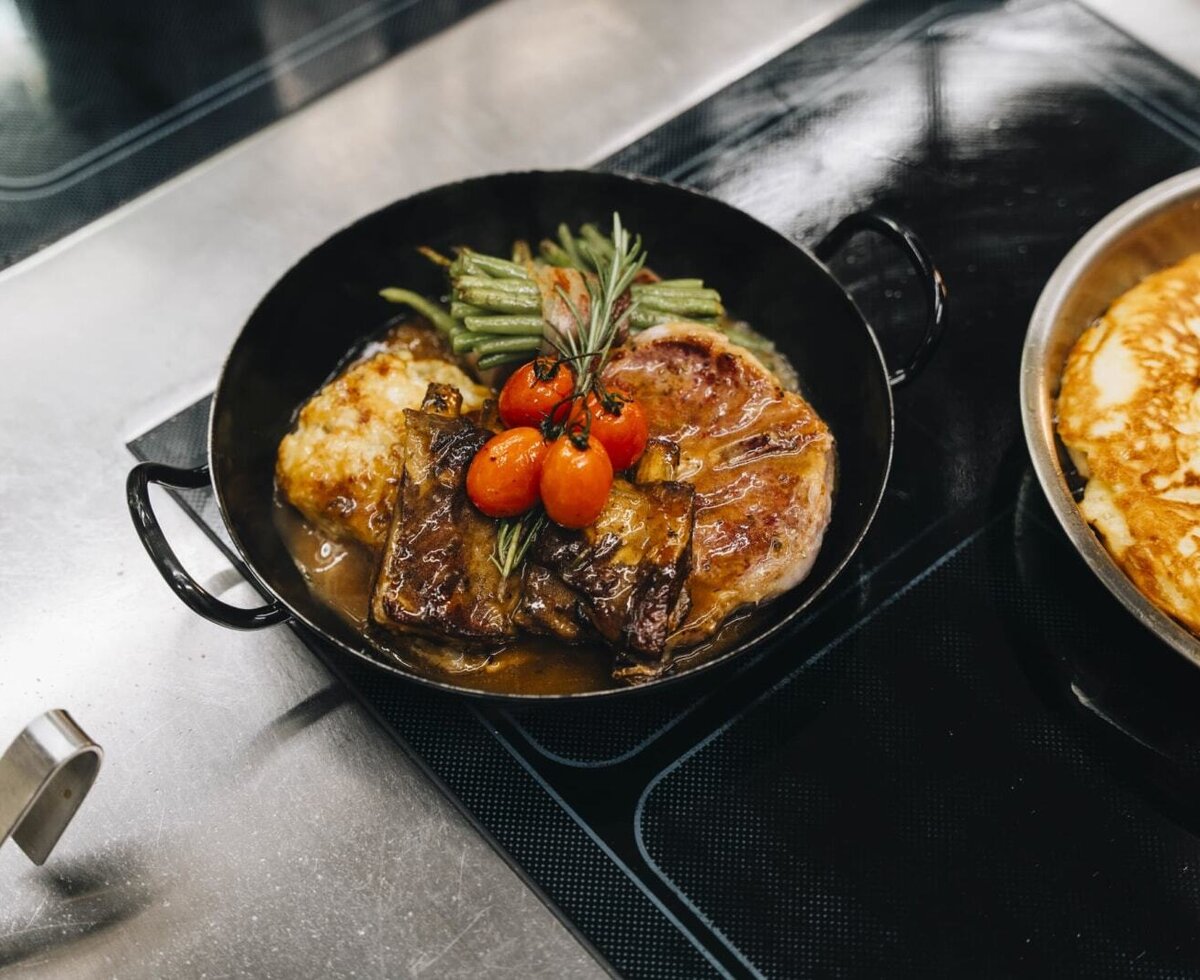 Hearty meat dish with ribs, potato side, green beans, and cherry tomatoes, served in a pan at the farmhouse.