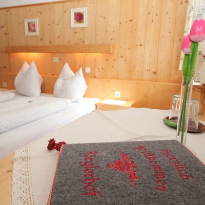Bedroom within the holiday apartment at the Farm House, featuring twin beds, wooden wall paneling with integrated lighting, and a table with a welcome guide.