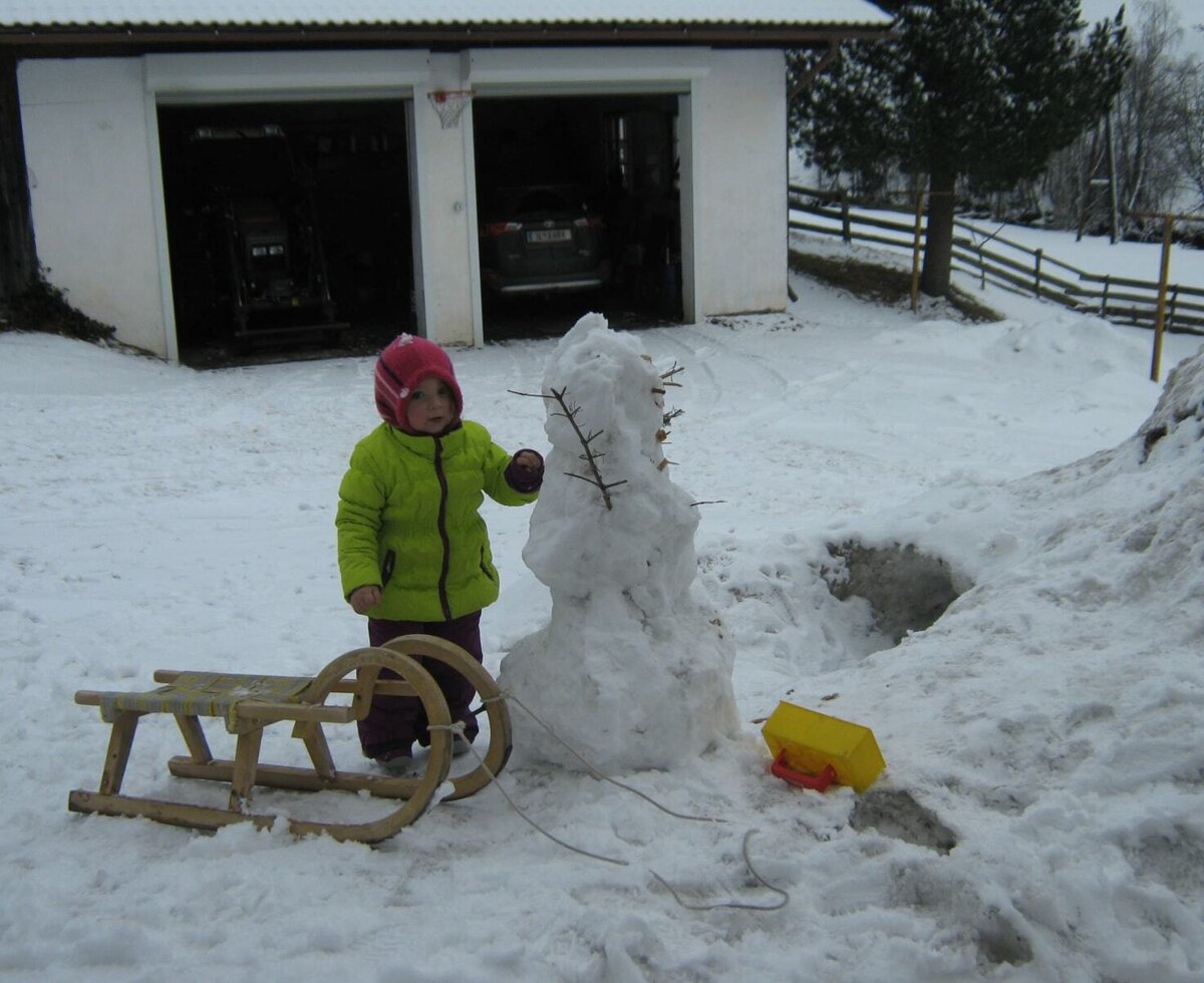 The snowy outdoor area of the Farm House, featuring a child playing with a snowman and a sled.
