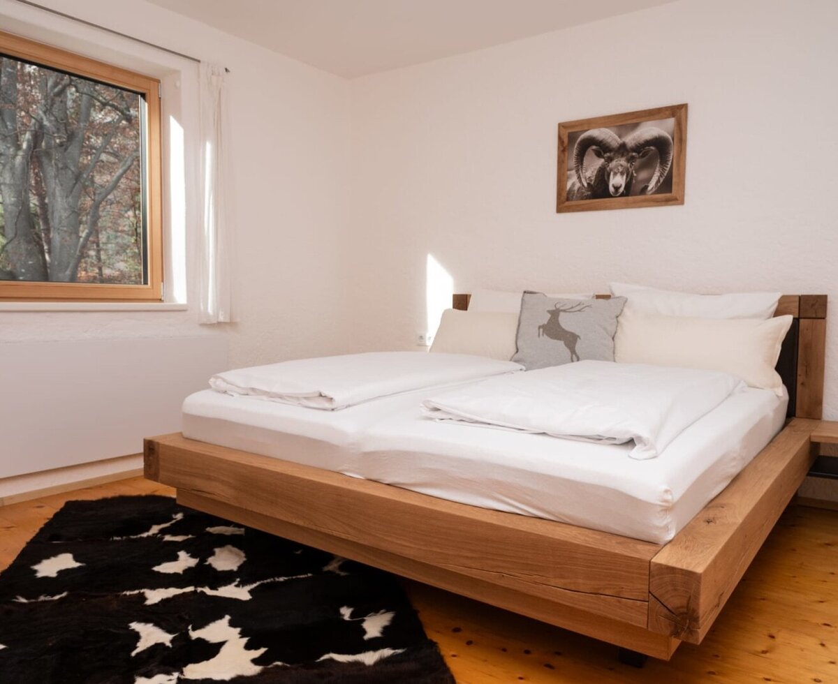 Bedroom in the apartment with a double bed, wooden floor, a black and white rug, and a window overlooking trees.