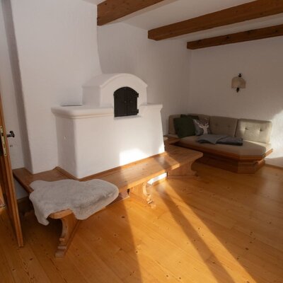 Living area of the Apartment featuring a traditional tiled stove, wooden bench, sofa, and exposed wooden beams.