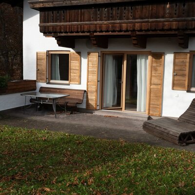 The Apartment's private terrace features an outdoor dining table, a bench, a wooden lounge chair, and direct access to a grassy area.