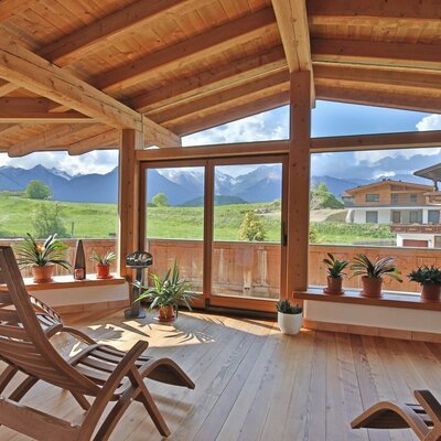 Relaxation area in the farmhouse with wooden lounge chairs and panoramic views of the mountains and surrounding landscape.