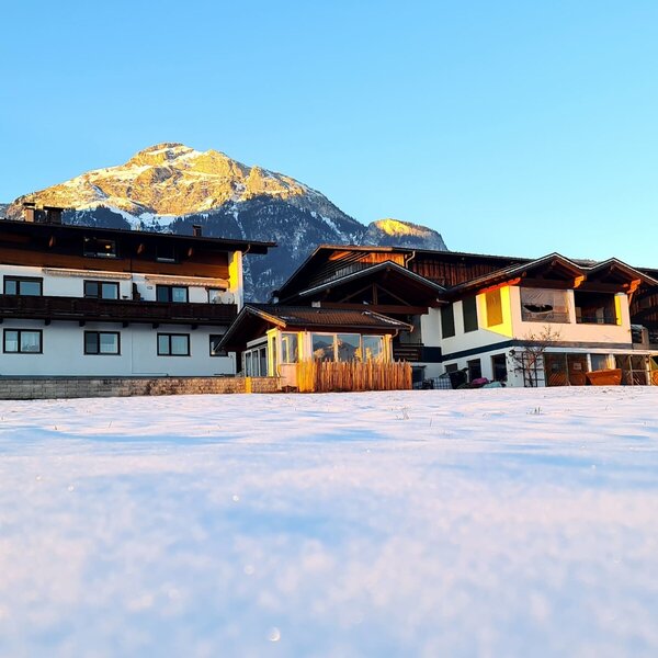 The Farm House exterior, showcasing its traditional design with multiple wooden balconies, situated in a snow-covered landscape with mountains visible in the background.