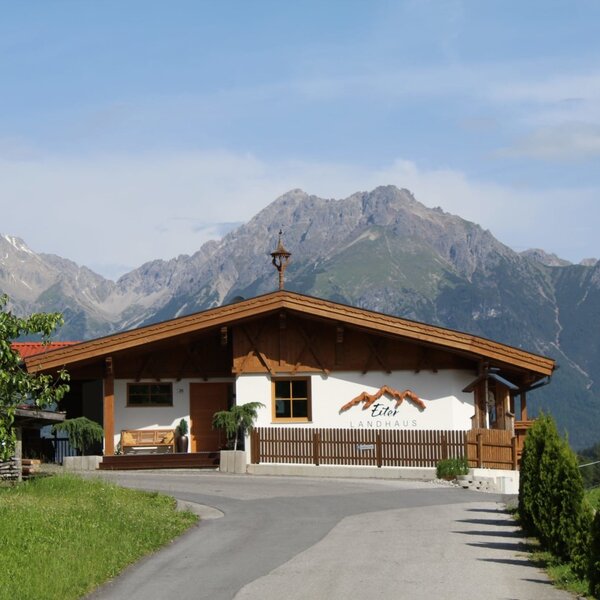 The exterior of the Ap­par­te­ments, featuring a traditional country house style, a mountain backdrop, and a driveway.