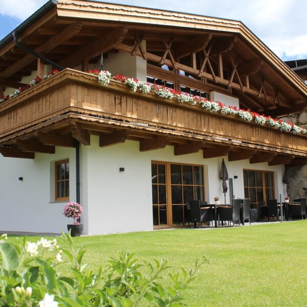 Exterior view of the Ap­par­te­ments featuring wooden balconies with flower boxes, a green lawn, and an outdoor seating area.