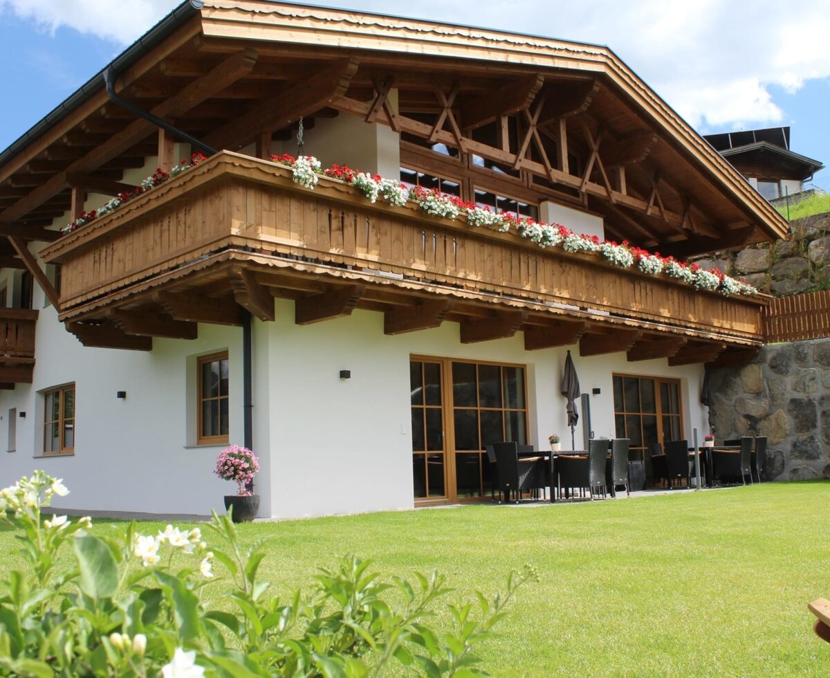 Exterior view of the Ap­par­te­ments featuring wooden balconies with flower boxes, a green lawn, and an outdoor seating area.