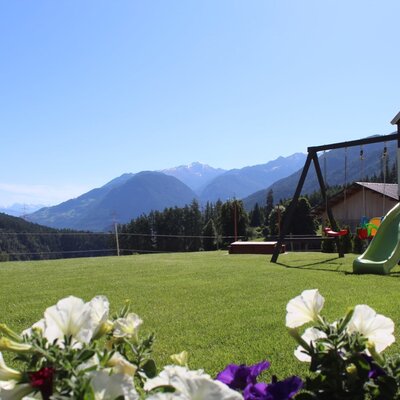 Green lawn with a children's playground and mountain views, part of the Ap­par­te­ments.