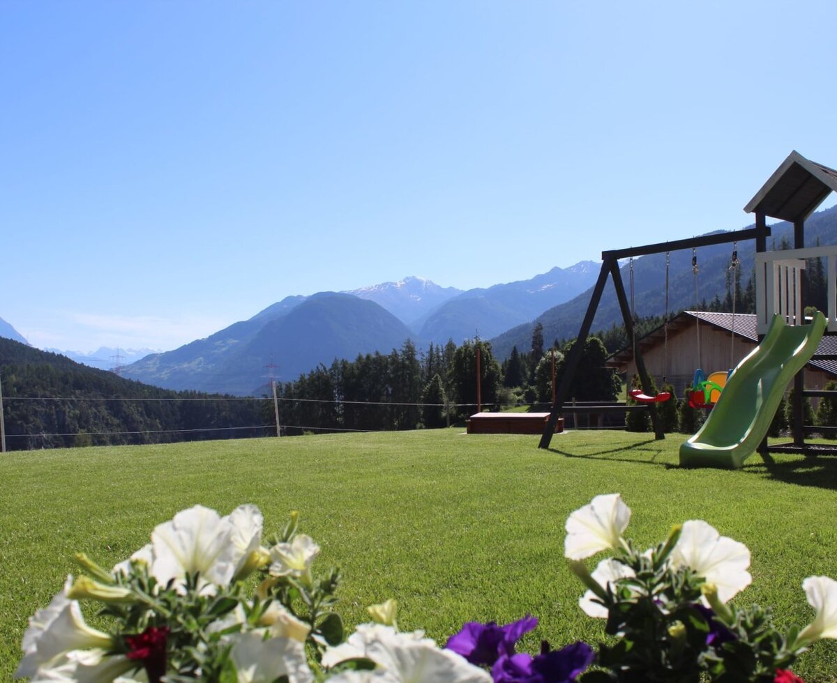 Green lawn with a children's playground and mountain views, part of the Ap­par­te­ments.