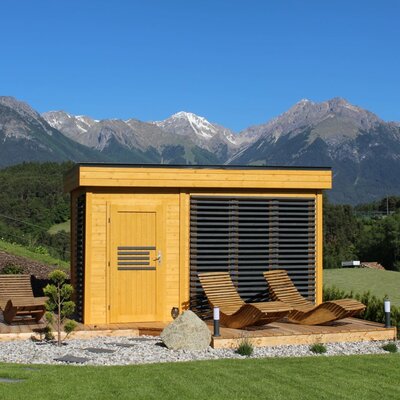 Outdoor sauna of the Ap­par­te­ments with a wooden terrace, lounge chairs, and mountain views.