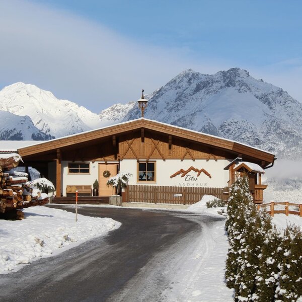 Exterior of the Ap­par­te­ments, featuring a wooden facade, snow-covered mountains in the background, and a driveway.