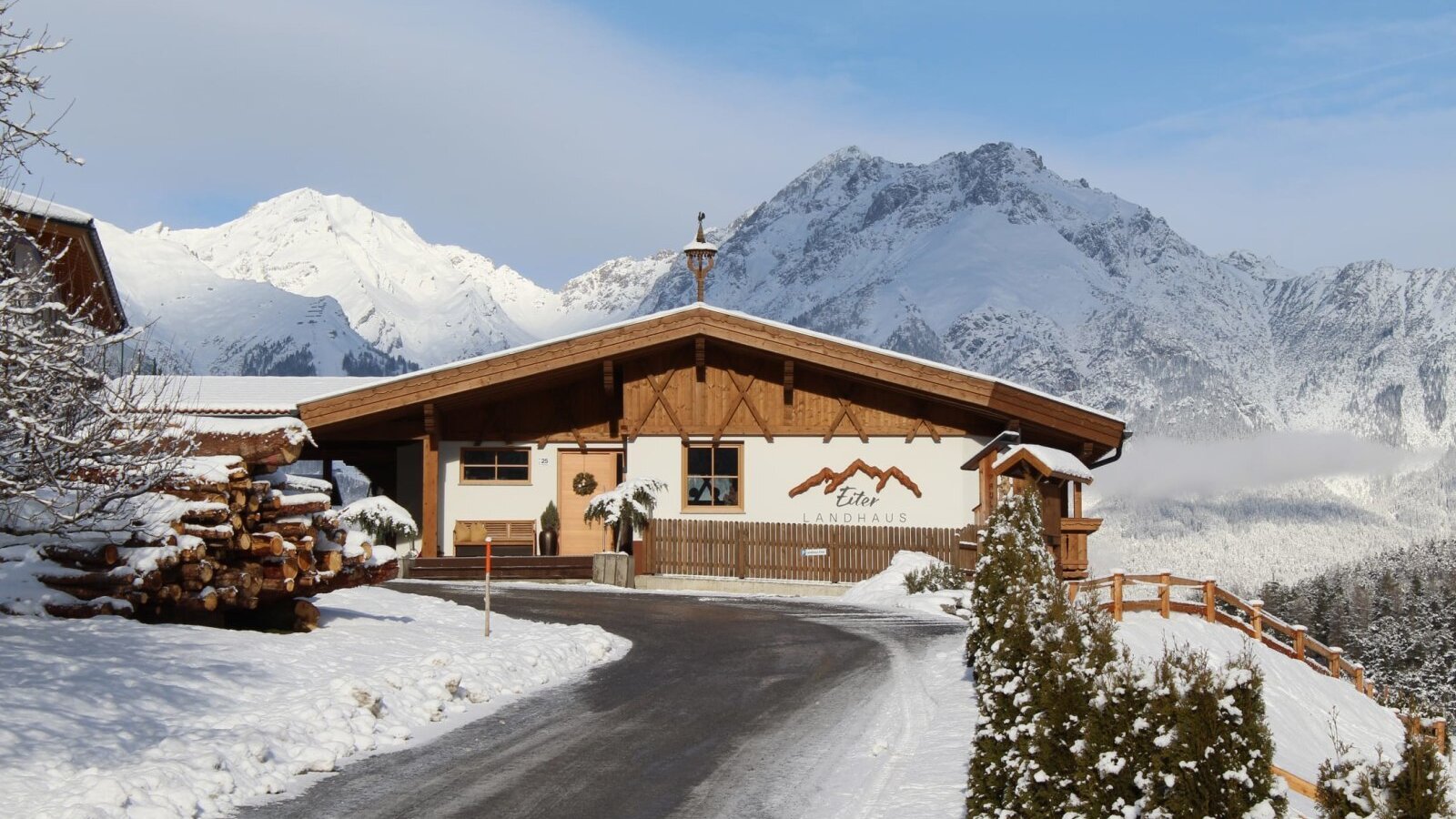 Exterior of the Ap­par­te­ments, featuring a wooden facade, snow-covered mountains in the background, and a driveway.