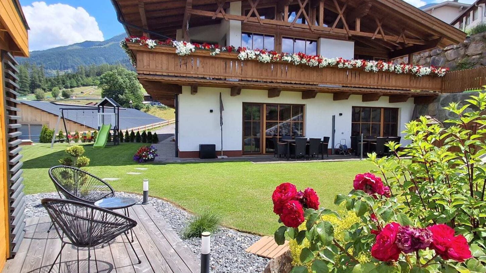 Exterior of the Ap­par­te­ments featuring balconies with flowers, a garden, outdoor seating, and a children's playground.